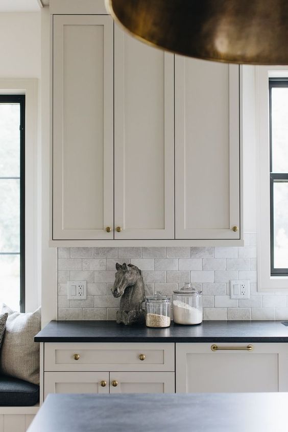 a modern farmhouse mushroom kitchen with shaker cabinets, black stone countertops, brass handles and knobs, a neutral tile backsplash