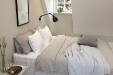 a modern greige attic bedroom with a bed, a nightstand and a black sconce, neutral and greige bedding, a small artwork is a cozy little sleeping space