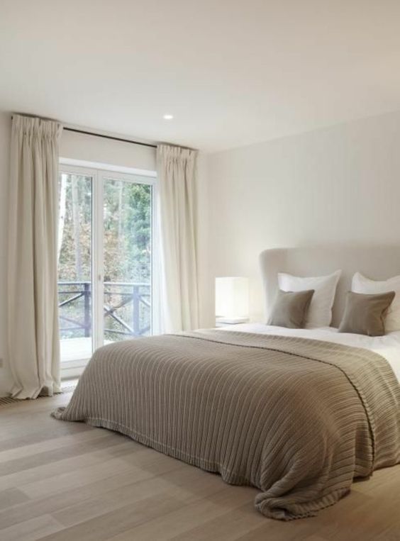 a neutral bedroom with a creamy upholstered bed, grey and white bedding, creamy curtains and a greige floor is very relaxing