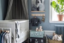 a pastel nursery in Scandi style with blue walls, a white crib, a dreamy artwork, some suitcases and a basket for storage and cool toys