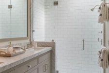 a pretty neutral bathroom clad with subway tiles, with a greige vanity with a white stone countertop and a skylight over the shower