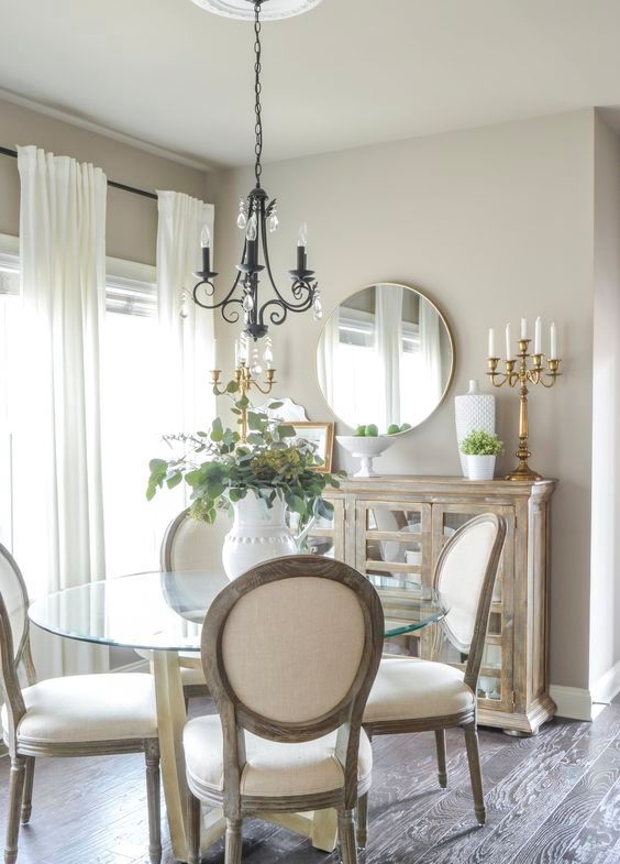 a refined greige dining nook with a reclaimed credenza, a glass round table, white chairs, a vintage chandelier and a chic candelabra