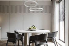 a sleek and refined minimalist dining room with greige walls, a round table, black chairs, round chandeliers and natural light