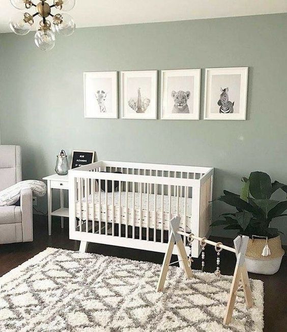 a soothing Scandi nursery with pale green walls, a white crib, a mini gallery wall, a potted plant, a neutral chair and a nightstand