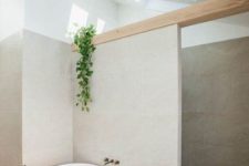 a stylish greige bathroom clad with large scale tiles, a wooden beam, a shower space, an oval tub an a wooden side table plus skylights