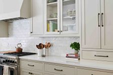 a stylish greige kitchen with white stone countertops, a white subway tile backsplash and black fixtures is chic and cool