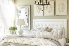 a vintage greige bedroom with a white upholstered bed, a white upholstered bench, a pretty gallery wall, some printed yet neutral bedding and textiles