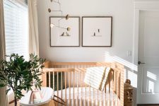 a welcoming Scandi nursery with stained furniture, a printed rug, a couple of artworks and a mobile, a basket for storage and a potted plant