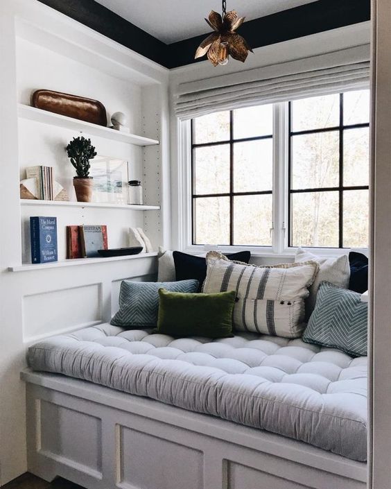 a welcoming and cozy reading nook by the window - a soft upholstered seat with drawers and some built-in shelves right here