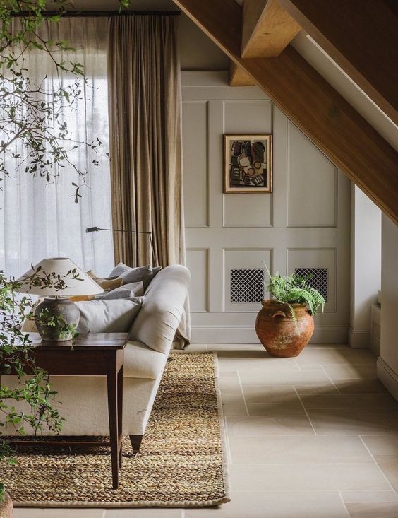 A welcoming greige living room with paneled walls, a neutral sofa, a dark stained coffee table, potted plants and a warm colored rug