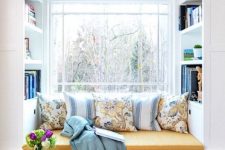 a window with a built-in storage unit with a seat, with built-in shelves and lots of pillows and a blanket is a lovely nook to read something