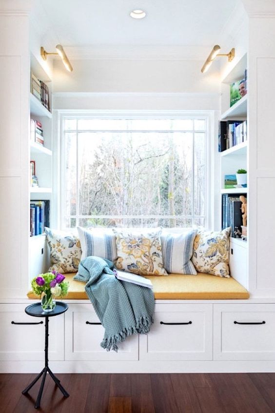 A window with a built in storage unit with a seat, with built in shelves and lots of pillows and a blanket is a lovely nook to read something