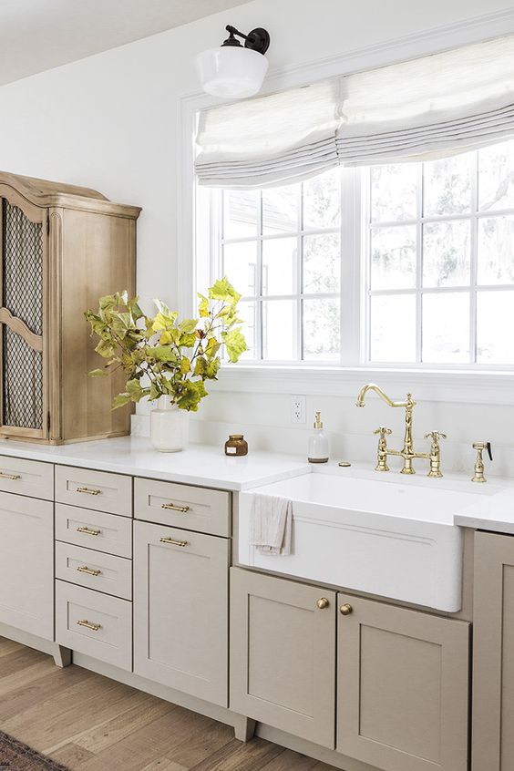 an elegant vintage greige kitchen with shaker cabinets, a white stone countertop and a backsplash, a wooden cabinet and gold fixtures