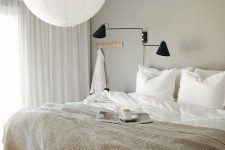 an ethereal greige bedroom with a creamy bed, a black sconce, a pendant lamp and neutral textiles is welcoming