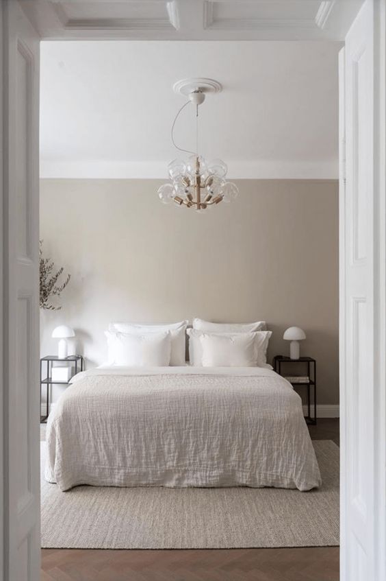 an ethereal greige bedroom with a white bed and neutral bedding, black nightstands and white table lamp plus a cool chandelier
