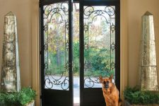 arched, wrought iron doors flanked by mirrored obelisks, with an arched window over the door and cool views of the garden through the doors