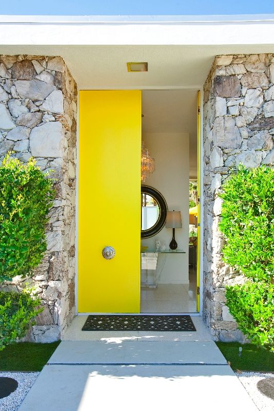 Sleek bold yellow double height doors with refined antique knobs is a gorgeous statement with both color and style of the doors