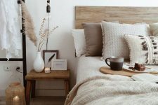 03 a neutral boho bedroom with a stained wooden bed, layered bedding, a wooden nightstand, candles, pampas grass and black touches