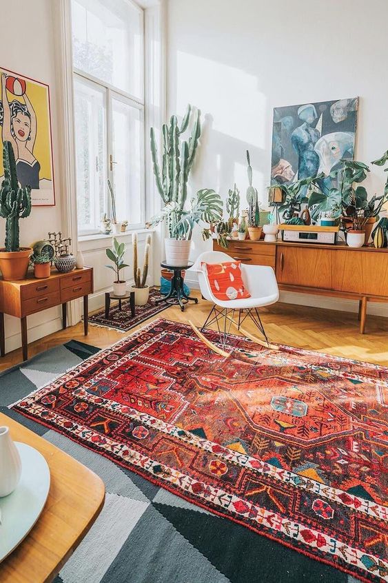 A bright mid century modern living room with bold mismatching rugs, statement potted cacti and succulents and bright artworks