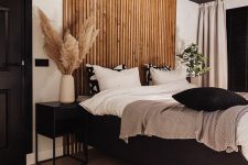 a chic and contrasting bedroom with a black ceiling, a wooden plank accent, a black floating bed and cool nightstands, a woven lamp and black and white bedding