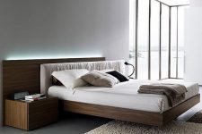 a laconic contemproary bedroom with a glazed wall, a stained floating bed with a lit up headboard and nightstands is a chic space