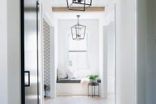 a light-filled entryway with a white planked ceiling, stained wooden beams, a light-stained floor, pendant lamps and a black sliding door