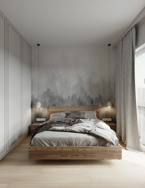 A neutral bedroom with a grey ombre accent wall, a floating light stained bed and nightstands, pendant lamps and grey bedding