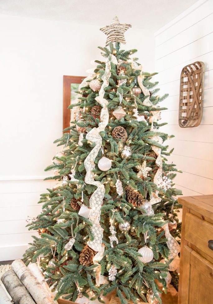 A lovely rustic or woodland Christmas tree with lace ribbons, pinecones, white ornaments, lights and animal shaped figurines
