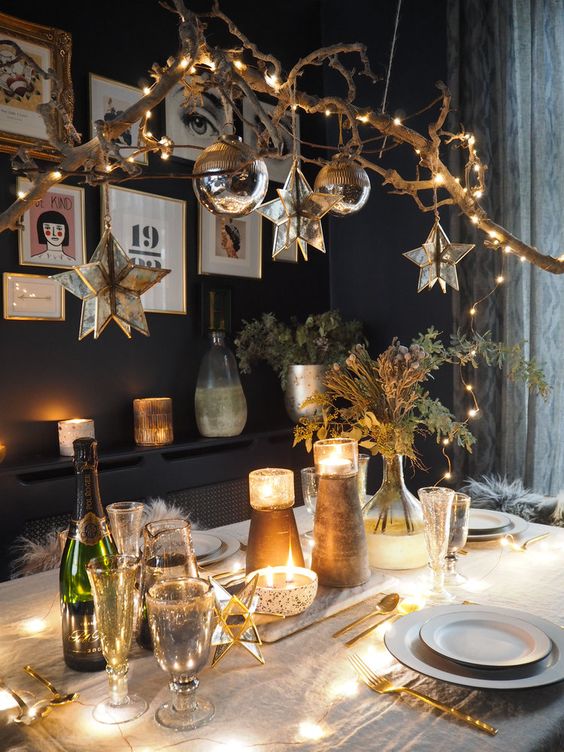 A woodland glam Christmas tablescape with shiny candleholders, greenery and a catchy chandelier made of a tree branch with lights, star and ball shaped ornaments