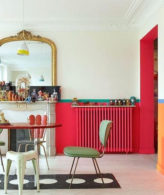 A bold vintage inspired interior with red touches including a radiator, green stools and chairs, a faux fireplace and an oversized mirror