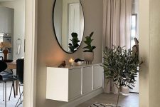 a greige entryway with a white console table, a round mirror, a potted tree and some matching greige curtains is a chic space