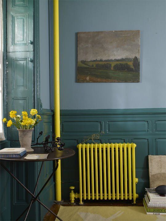 A moody vintage inspired space with blue walls and dark green wainscoting, a neon yellow radiator and a tube, bold blooms