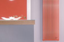 a neutral grey space with an orange accent wall and a vertical wall radiator that matches in color and gives a bold touch to the space