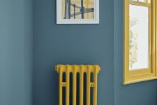 a slate blue space with a sunny yellow window frame and a matching radiator is a lovely and bold space with a contrasting touch