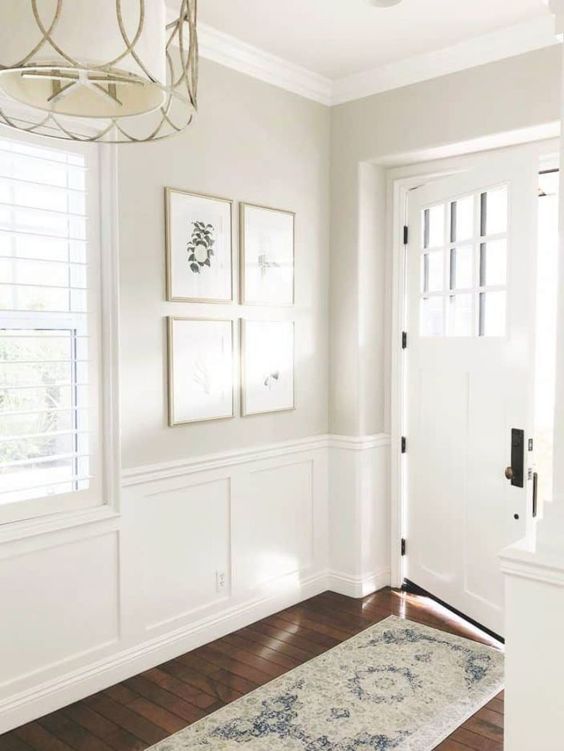 An airy and light filled greige entryway with white wainscoting, a chandelier, a mini gallery wall and a white door