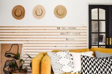 04 a chic living room with wooden slabs on the wall, a yellow sofa and graphic pillows, hats on display and some plants