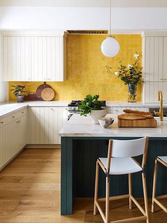 A chic vintage inspired kitchen with white beadboard cabinets, white stone countertops, a sunny yellow tile backsplash and a hunter green kitchen island