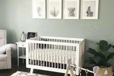 19 a cozy and cute nursery with a sage green accent wall, white furniture, a potted plant, a chic chandelier and a lovely printed rug