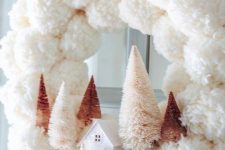 a delicate white pompom Christmas wreath with blush and rustic bottle brush trees and a mini house plus a mauve bow