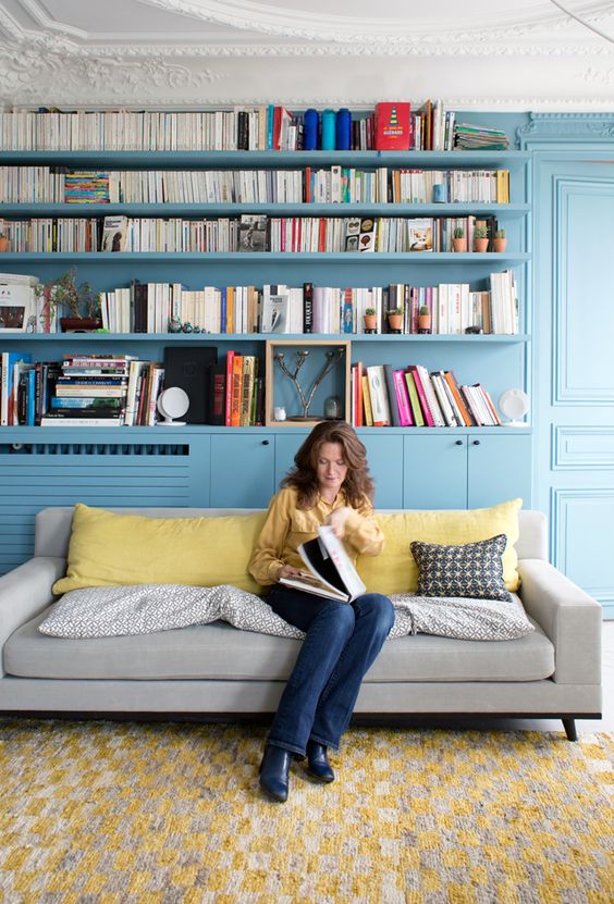 A living room and library done in stone blue   all the walls, shelves and storage units plus yellow accents in the space