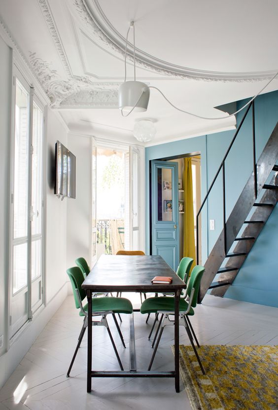 a catchy dining space with a stone blue accent wall, a black table and green retro chairs, a pendant lamp