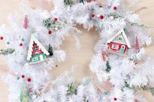 33 a white evergreen Christmas wreath with colorful pompoms, colorful small houses and bottle brush Christmas trees
