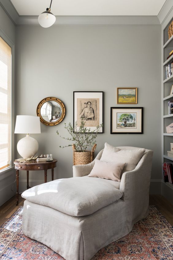 A lovely reading nook in dove grey, with a built in bookcase, a neutral lounger, a mini gallery wall and a vintage side table