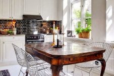35 a white eat-in kitchen with a black tile backsplash, a rich-stained dining table and modern wire chairs for a contrast