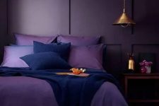 36 a moody monochromatic bedroom with a deep purple paneled wall, purple and navy bedding, a wooden nightstand and a metal pendant lamp