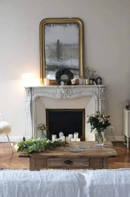 a beautiful living room with a French fireplace, a stained wood coffee table, a white sofa, a mirror in a shiny frame and candles