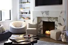 a beautiful living room with built-in shelves, black and white chairs, a living edge coffee table, a white marble fireplace