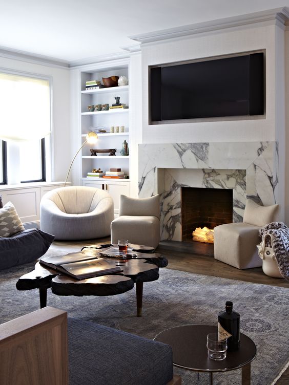 a beautiful living room with built-in shelves, black and white chairs, a living edge coffee table, a white marble fireplace