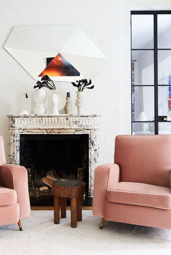 a bold and edgy space with a marble clad fireplace, pink chairs, a side table, white vases on the mantel and a cool mirror