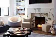 a chic modern living room in neutrals, with a faux fireplace clad with white marble and lit up firewood inside it